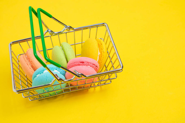 French macarons cookies in shopping basket on yellow background - Foto, afbeelding