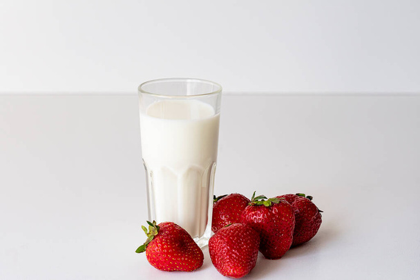 Een glas verse melk en verse rijpe aardbeien Verse biologische yoghurt met aardbeien op witte achtergrond. - Foto, afbeelding