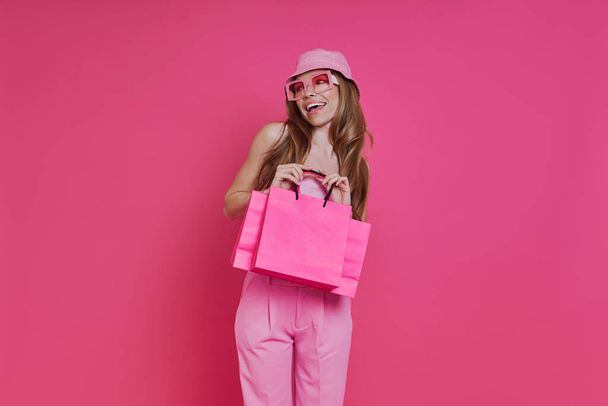 Excited young woman carrying shopping bags while standing against pink background - Foto, immagini