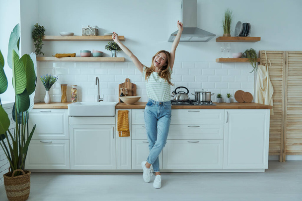 Full length of beautiful young woman looking happy while standing at the domestic kitchen - Valokuva, kuva
