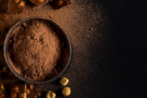Broken chocolate nuts pieces and cocoa powder on dark background - Φωτογραφία, εικόνα