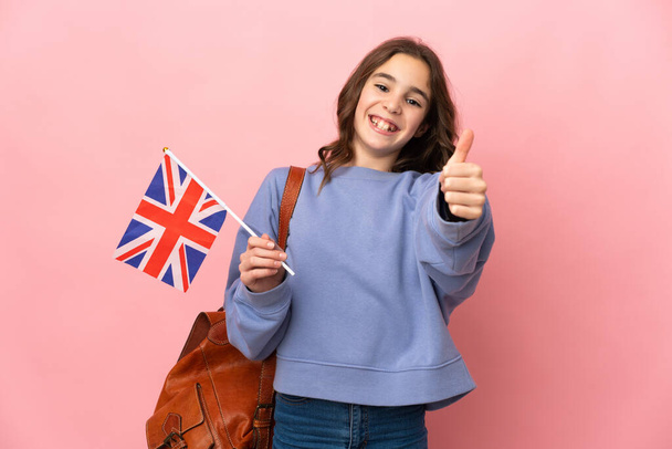 Kleines Mädchen mit einer Flagge des Vereinigten Königreichs auf rosa Hintergrund und Daumen hoch, weil etwas Gutes passiert ist - Foto, Bild