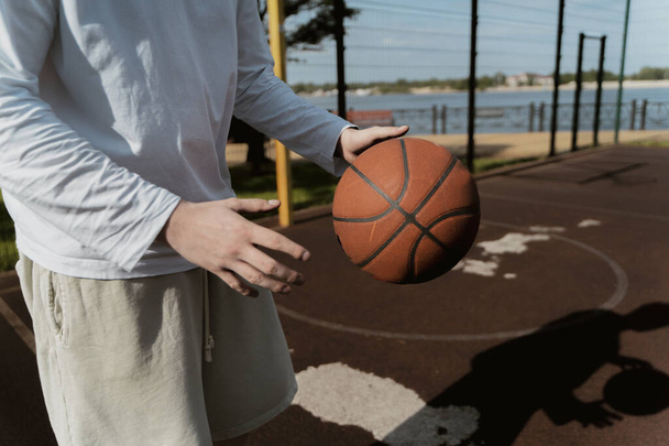 der Kerl hält auf der Straße auf dem Basketballplatz einen Basketball in den Händen - Foto, Bild