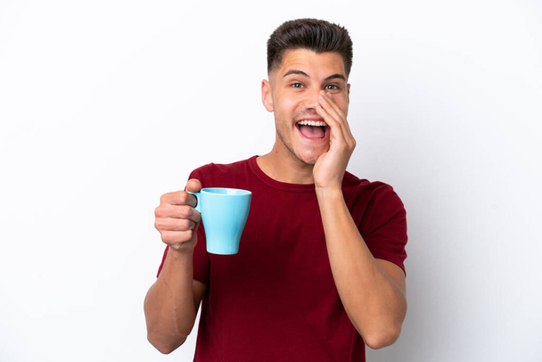 Young caucasian man holding cup of coffee isolated on white background shouting with mouth wide open - Фото, изображение