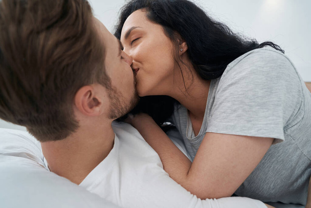 Woman in love lying on man in bed and giving him kiss - Foto, afbeelding