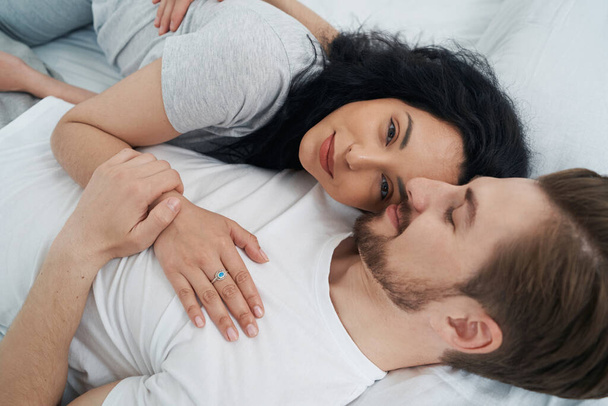 Romantic young man hugging his beloved woman lying beside him in bed - Φωτογραφία, εικόνα