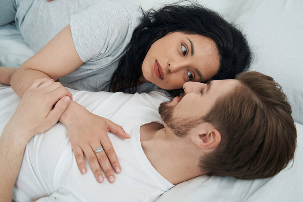 Romantic woman lying beside beloved person in bed and looking into his eyes - Фото, зображення