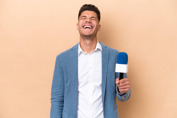 Mladý kavkazský televizní moderátor muž izolovaný na bílém pozadí se směje - Fotografie, Obrázek