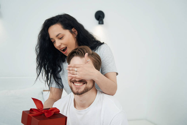 Smiling woman presenting gift to young male while covering his eyes with her hand - Фото, зображення