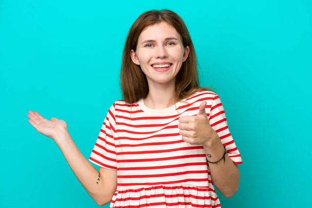 Young English woman isolated on blue background holding copyspace imaginary on the palm to insert an ad and with thumbs up - Foto, immagini