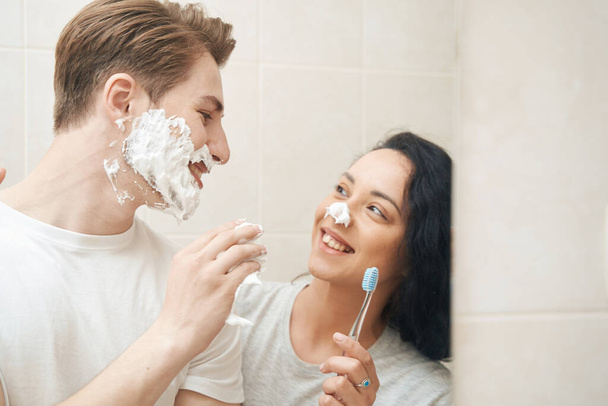 Cheerful man applying shaving foam to face of his pleased female companion - Foto, afbeelding