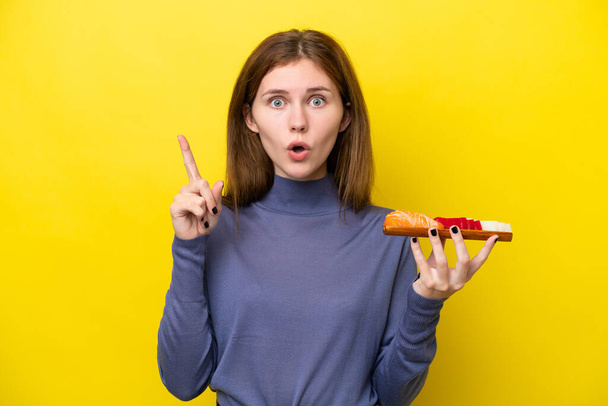 Joven mujer inglesa sosteniendo sashimi aislado sobre fondo amarillo con la intención de realizar la solución mientras levanta un dedo - Foto, Imagen