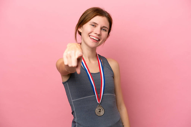 Giovane donna inglese con medaglie isolate su sfondo rosa punta il dito contro di te con un'espressione sicura - Foto, immagini