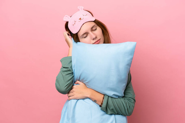 Giovane donna inglese in pigiama isolato su sfondo rosa in pigiama e tenendo un cuscino durante il sonno - Foto, immagini