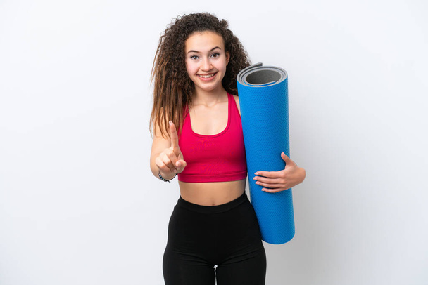 Young sport Arab woman going to yoga classes while holding a mat isolated on white background showing and lifting a finger - Фото, изображение