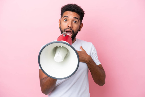Young Brazilian man isolated on pink background shouting through a megaphone with surprised expression - Fotografie, Obrázek