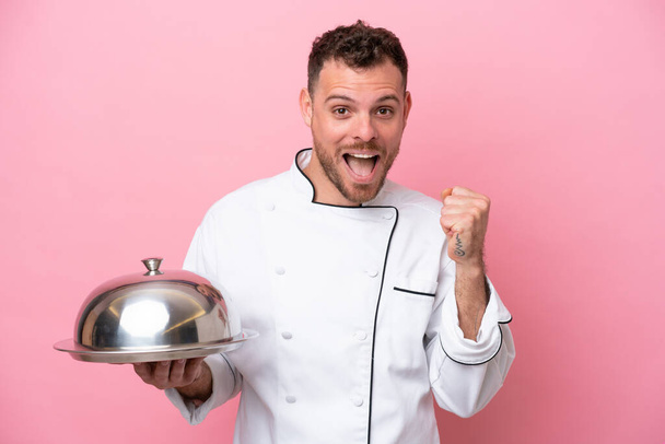 Young Brazilian chef with tray isolated on pink background celebrating a victory in winner position - Zdjęcie, obraz