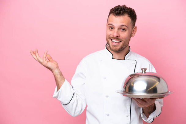 Giovane chef brasiliano con vassoio isolato su sfondo rosa allungando le mani a lato per invitare a venire - Foto, immagini