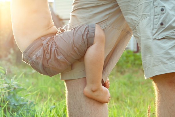 Малыш играет со своим отцом и держит его за ноги
 - Фото, изображение