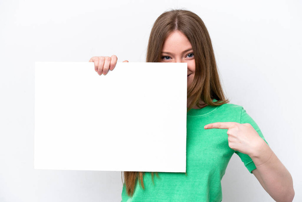 Νεαρή καυκάσια γυναίκα απομονωμένη σε λευκό φόντο κρατώντας ένα άδειο πλακάτ και κρυμμένη πίσω του - Φωτογραφία, εικόνα