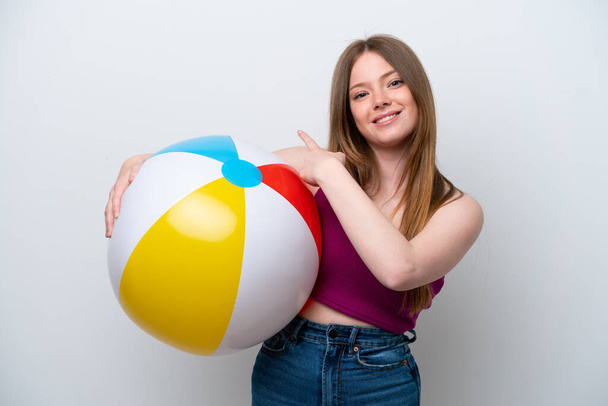 Young caucasian woman holding beach ball isolated on white background pointing back - Fotoğraf, Görsel