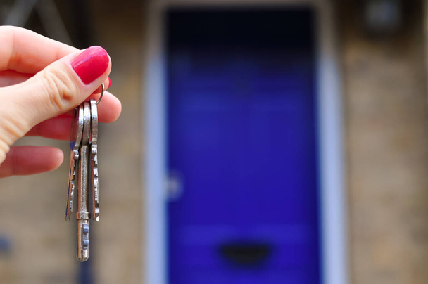 Womans hand with metal keys on blurred background with house. High quality photo - Photo, Image