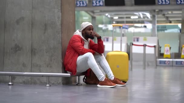 Fáradt afro-amerikai férfi feldúlt a repülőtéren a járata késik. Ideges utazó férfi vár egy repülőre az üres terminálon, csomagokkal. Kimerült fickó egy hosszú éjszakai kapcsolaton a reptéren. - Felvétel, videó