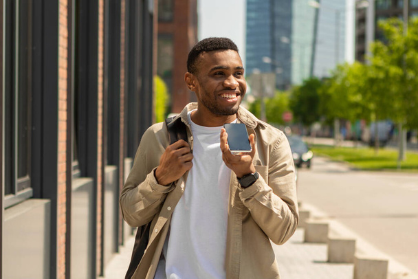 Черный мужчина разговаривает по мобильному телефону в громкоговоритель, идущий по улице. Высокое качество фото - Фото, изображение