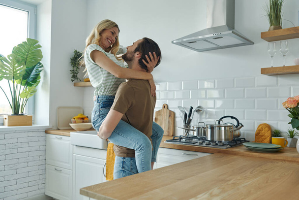 Hermosa pareja joven abrazando y divirtiéndose en la cocina doméstica - Foto, Imagen