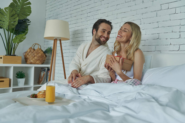 Happy woman receiving a gift box from her boyfriends while both sitting in bed - Foto, immagini