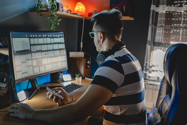 Vista posterior de un hombre caucásico adulto sentado en la mesa de PC de la computadora en casa mirando a la pantalla del monitor con el gráfico de comprobación de criptomonedas mercado de tipo de cambio y la minería de inversión personas reales - Foto, Imagen