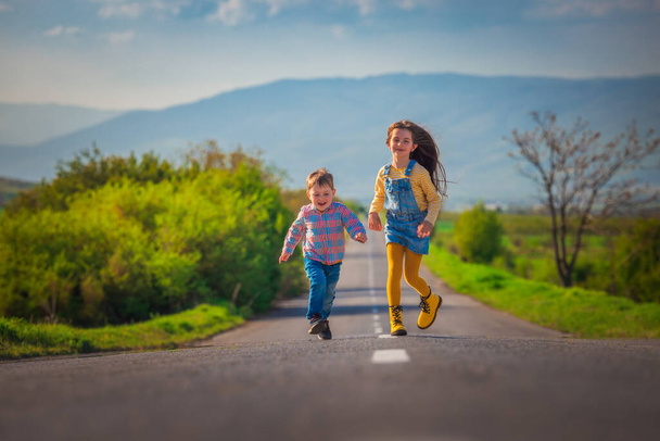 Glückliche Kinder Bruder und Schwester laufen auf der Straße in der Landschaft. Glück, Freiheit und Kindheitskonzept. - Foto, Bild