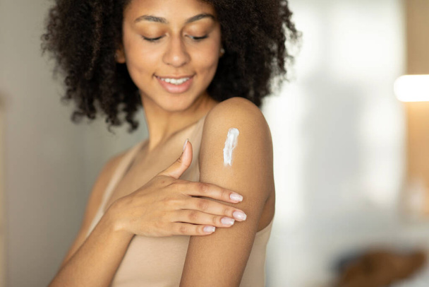 Vrouw die hydraterende lotion of crème op haar schouders aanbrengt, thuis voor haar huid zorgt, in de badkamer staat. Hoge kwaliteit foto - Foto, afbeelding