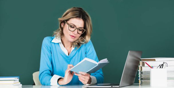 Female attractive teacher. Portrait of smart young woman in glasses with book on the blackboard in class at high school or college. Female student study in university - Foto, afbeelding