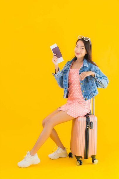 Портрет красива молода азіатка з багажною сумкою з паспортом і квитком на посадковий талон на жовтому ізольованому тлі
 - Фото, зображення