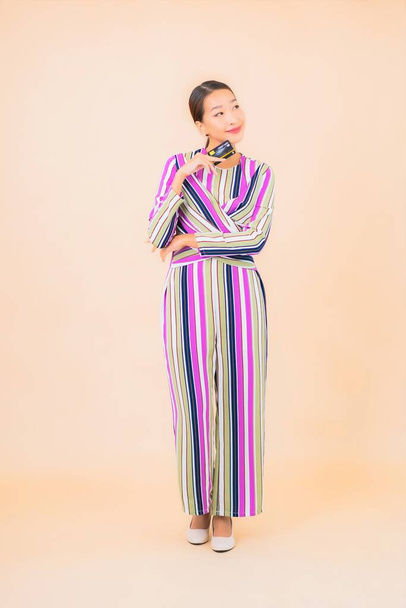 Portrét krásná mladá asijská žena s chytrým mobilním telefonem a kreditní kartou na barevném izolovaném pozadí - Fotografie, Obrázek