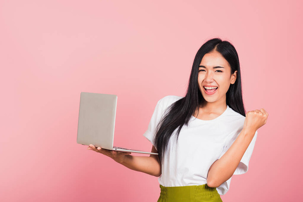 Portrait of happy Asian beautiful young woman teen confident smiling face holding using laptop computer and excited celebrating success, studio shot isolated on pink background, with copy space - Foto, immagini
