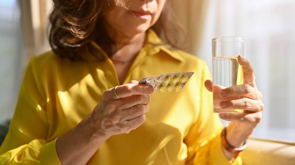 Malata donna asiatica di età compresa tra un bicchiere d'acqua e un pacchetto di pillole nel suo soggiorno. Concetto di assistenza sanitaria e problemi sanitari. immagine ritagliata - Foto, immagini