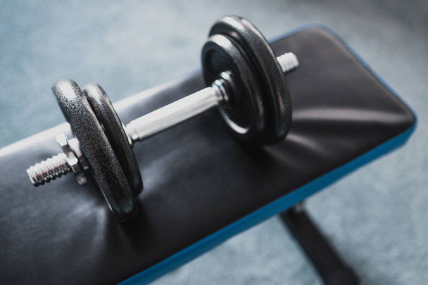home gym and fit lifestyle still-life, room with flat abs bench and dummbell on top of it shot at shallow depth of field with desaturated moody tones - Fotoğraf, Görsel