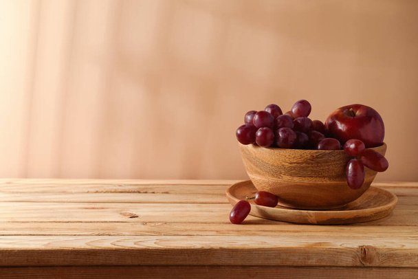 Grapes and red apple in wooden bowl over beige background. Summer kitchen table mock up for design and product display - Fotografie, Obrázek