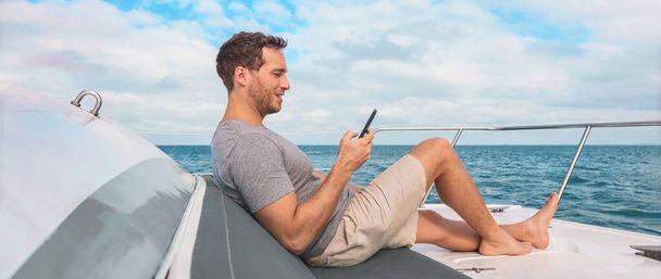 Phone using on cruise ship. Man luxury travel texting with data on yacht boat relaxing on deck banner panoramic. Caribbean vacation. - Foto, Imagen