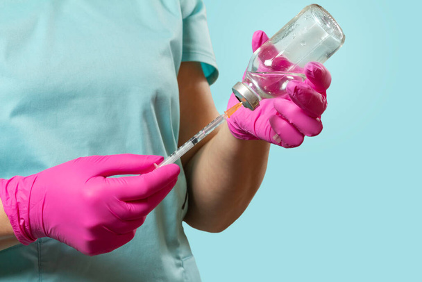 Frasco de vidro para medicamento líquido e uma seringa de plástico para injeção em mãos com luvas de látex. - Foto, Imagem