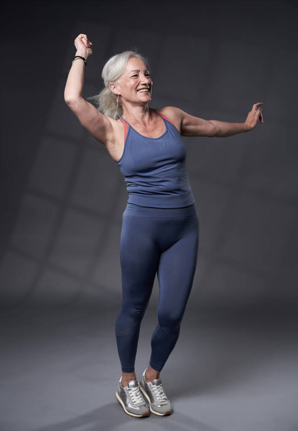 Senior woman with white hair working out a fitness class, on grey background - Fotó, kép