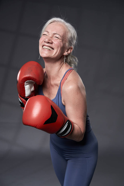 Femme âgée aux cheveux blancs prenant des cours de boxe, en gants rouges - Photo, image