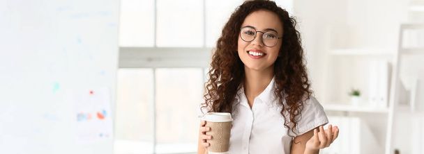 Portrait of beautiful African-American businesswoman with cup of coffee in modern office - Photo, image