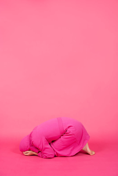 Child down on knees and wearing housecoat isolated on pink background. Anxiety and depression abstract concept with copy space. - Photo, Image