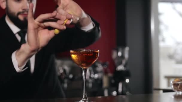 Profesionální barman v černém obleku rozprašuje chutný alkoholický nápoj ve skle pro dekoraci. Kavkazský vousatý muž servírující koktejl s jedinečným receptem na barovém pultu. - Záběry, video