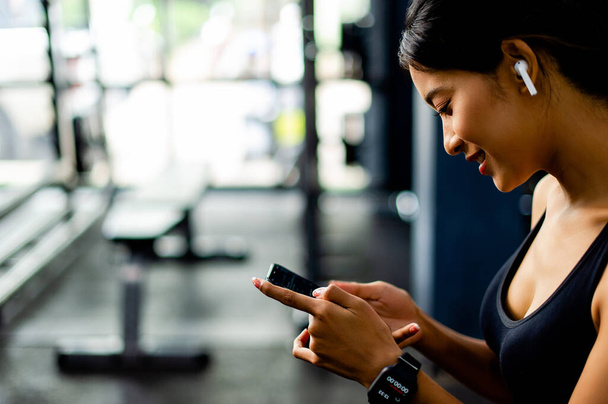 Mujer asiática en el gimnasio y jugando por teléfono mientras escucha música antes de hacer ejercicio en el gimnasio - Foto, Imagen