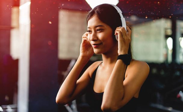 Asian woman in the gym and listen to music before exercising in the fitness center young women love health and beauty - Фото, зображення