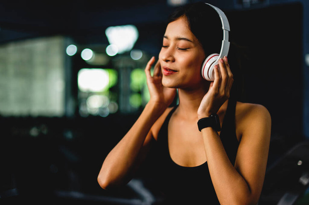 menina no ginásio exercício Ouvir música com fones de ouvido branco sobre-ouvido e usando um temporizador de batimento cardíaco digital. exercício sistemático Os exercícios são estruturados. - Foto, Imagem